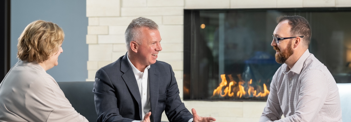 Three Twin Feathers employees sit around table with fireplace in background and discuss marketing strategy.