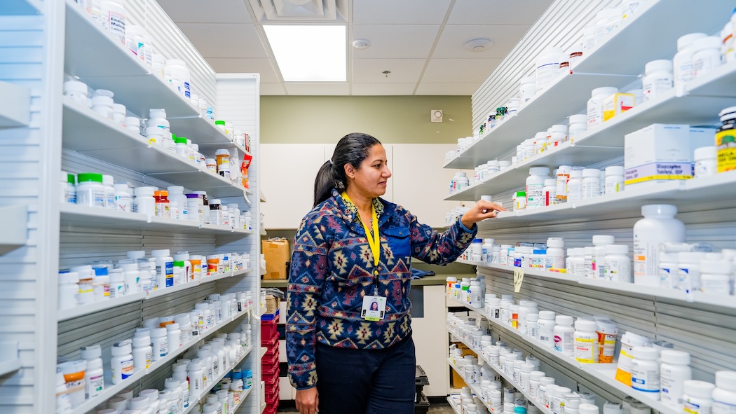 Pharmacist looking at shelves of medicine at HCHC