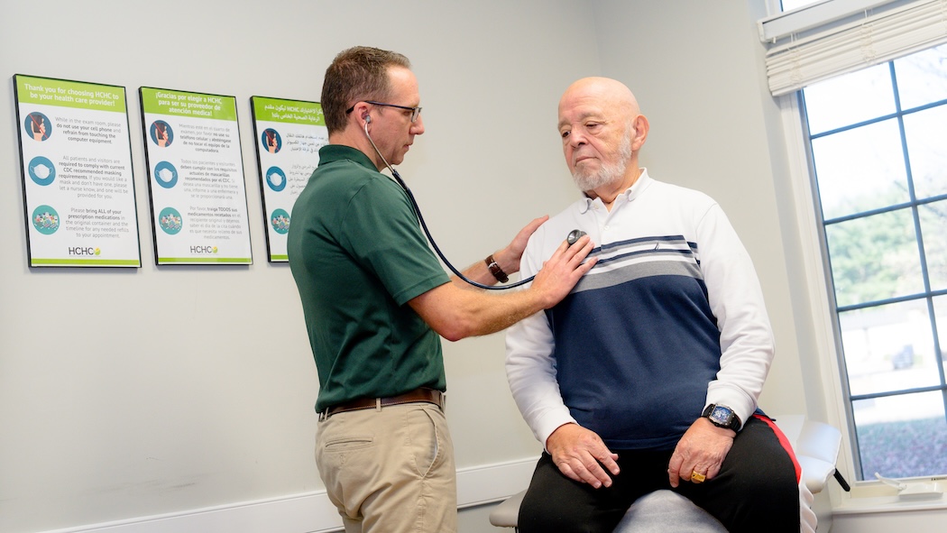 Male healthcare provider using a stethoscope on an older patient's chest.